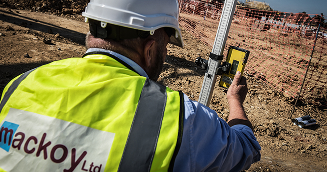 Mackoy Ltd Civil Engineering Groundworker in Branded Vest Measuring on Site