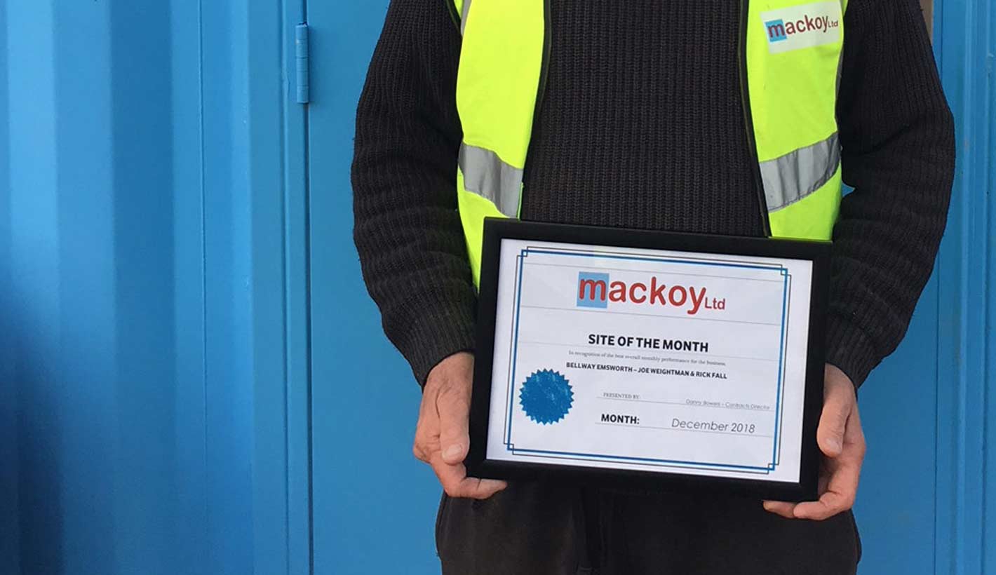 Site of the Month award held by Groundworks Foreman on front of blue container